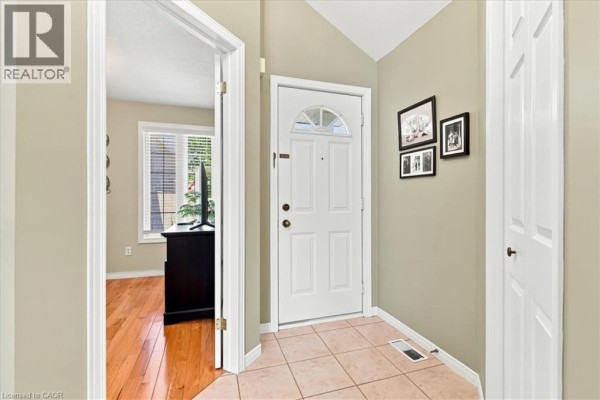 Interior hallway with beige walls, tiled floor, white front door, and photos. - 1550 Gordon Street Unit# 18, Guelph