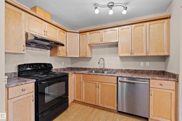 Kitchen details with light wood cabinets, black stove, and stainless steel dishwasher against a beige wall. - 15504 102 Av Nw, Edmonton