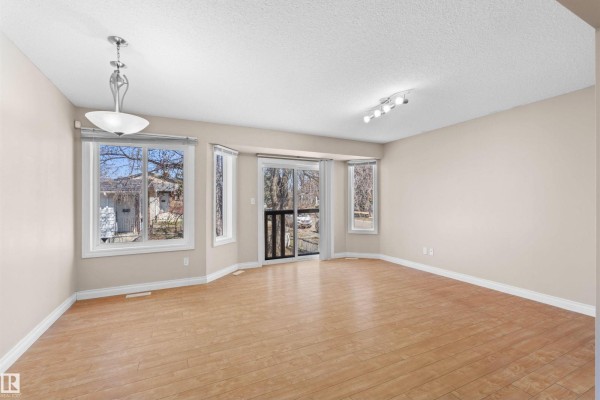 Living room with light wood floors and beige walls, opening to a kitchen area with light wood cabinets. - 15504 102 Av Nw, Edmonton