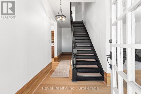 Interior foyer with a dark wooden staircase, white walls, and light wood flooring. - 15578 Simcoe Street, Scugog