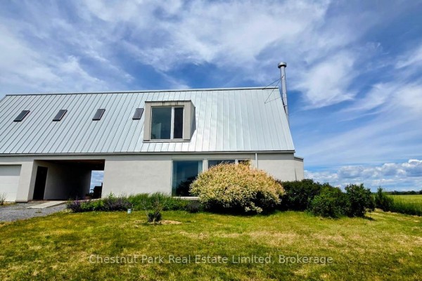 Close-up of the modern house showing a metal roof, windows, and surrounding green lawn. - 1558 Gilead Road, Prince Edward County