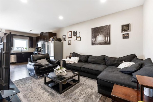 Living room with a dark grey sectional sofa, black leather armchair, and open kitchen. - 156 1655 Leila Avenue, Winnipeg