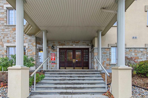 Building entrance with stone facade, double wooden doors, and concrete stairs. - 156 Boul. De Lucerne, #303, Gatineau