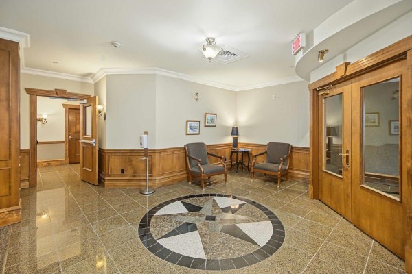 Lobby seating area with chairs, table, wooden paneling, and compass floor design. - 156 Boul. De Lucerne, #303, Gatineau