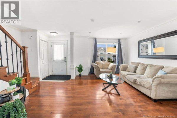 Living room with hardwood floors, a beige sofa, armchair, glass coffee table, and large mirror. - 156 Houlahan Street, Dieppe