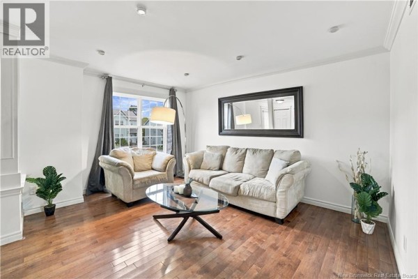 Living room with hardwood floors, beige sofa and armchair, glass coffee table, and large mirror. - 156 Houlahan Street, Dieppe