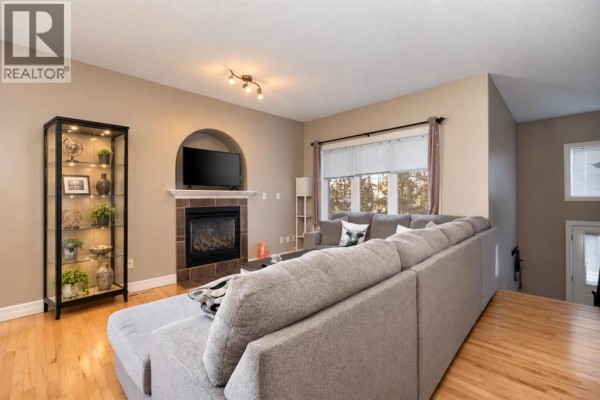 Living room with a sectional sofa, fireplace with a TV above, and display cabinet. - 156 Paris Crescent, Fort Mcmurray
