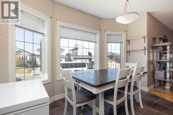 Dining area with a table, chairs, and large windows overlooking a residential street. - 156 Paris Crescent, Fort Mcmurray
