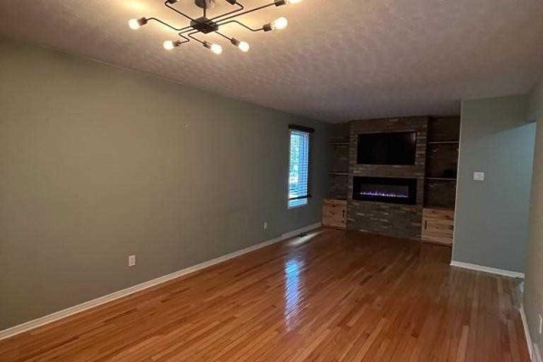 Living room with hardwood floors, a modern light fixture, and a stone fireplace with a television. - 156 Pochard Lane, London East