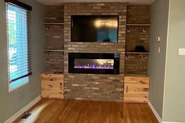 Close-up of a living room stone fireplace, television, and built-in wooden cabinets. - 156 Pochard Lane, London East
