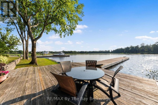 Outdoor dining set on a wooden deck overlooking the water and a boat dock. - 156 Prisque Road, Georgian Bay