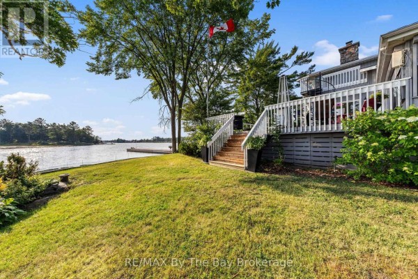 Side view of a multi-level house with a wooden deck and stairs leading down to a grassy lawn. - 156 Prisque Road, Georgian Bay