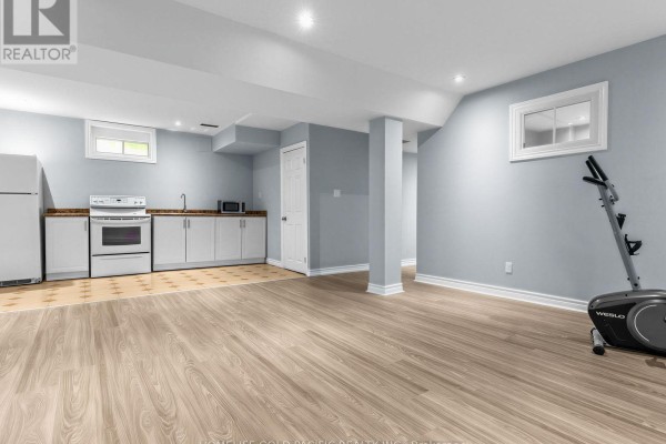 Basement with kitchenette, white cabinets, oven, microwave, wood-look floors, elliptical - 156 Ravenscroft Road Ajax