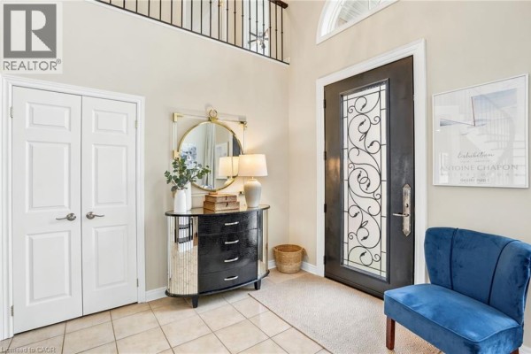 Foyer with a black dresser, round mirror, blue chair, and tiled floor. - 156 Valmont Street, Ancaster