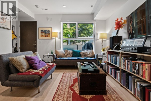Living room with sofa, coffee table, bookshelf, and large window. - 156 W Woodstock Avenue, Vancouver