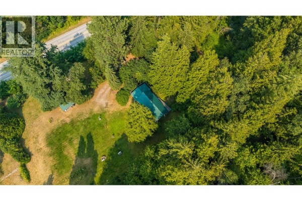 Aerial view of the property showing a house with a green roof surrounded by a large, wooded area and a road. - 1562 Arrow Lakes Drive, Castlegar