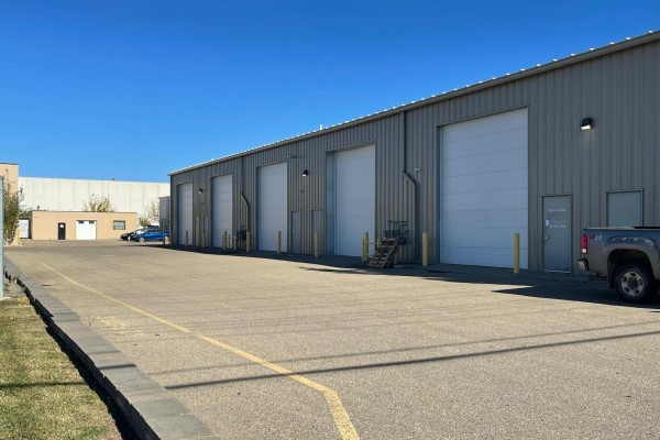 Exterior of a warehouse with multiple large white roll-up doors and smaller access doors. - 15634 - 112 Avenue Nw, Edmonton