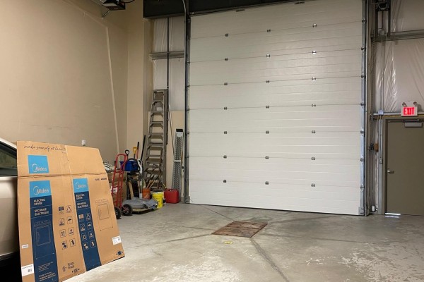 Interior view of a garage bay with a white roll-up door, ladder, and stored items. - 15634 - 112 Avenue Nw, Edmonton
