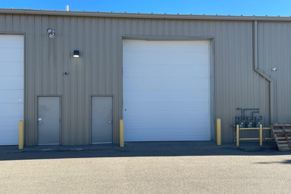 Side view of a commercial building with a large white roll-up door and two smaller metal doors. - 15634 - 112 Avenue Nw, Edmonton