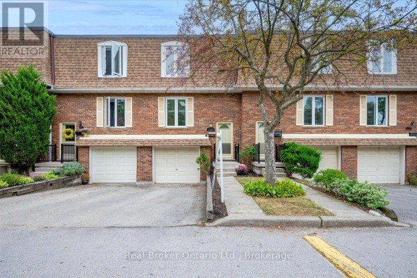 Front exterior of brick townhouse with attached garages and mature trees in the landscaping. - 1569 Westminster Place, Burlington