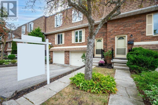 Front view of brick townhouses with garages, front doors, and a tree in the foreground. - 1569 Westminster Place, Burlington