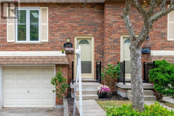 Close-up of townhouse exterior with red brick, beige front doors, and garages. - 1569 Westminster Place, Burlington