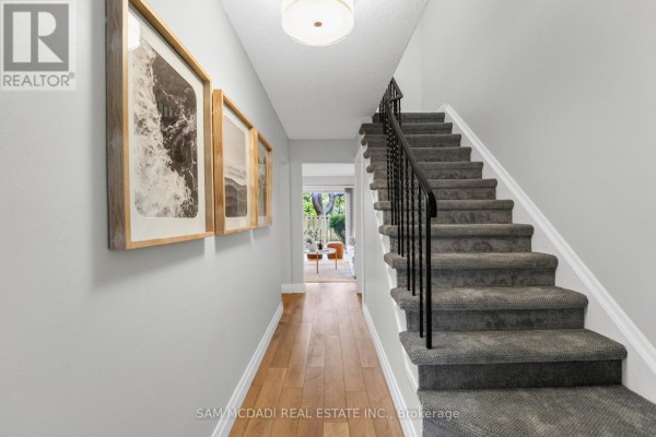 Hallway interior with wood flooring, grey carpeted stairs, black railing, and artwork on the left wall. - 157 - 400 Mississauga Valley Boulevard, Mississauga