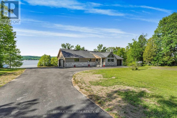 Exterior view of a modern house with a large driveway, green lawn, and lake in the background. - 157 Concession 1 Road, Alfred And Plantagenet