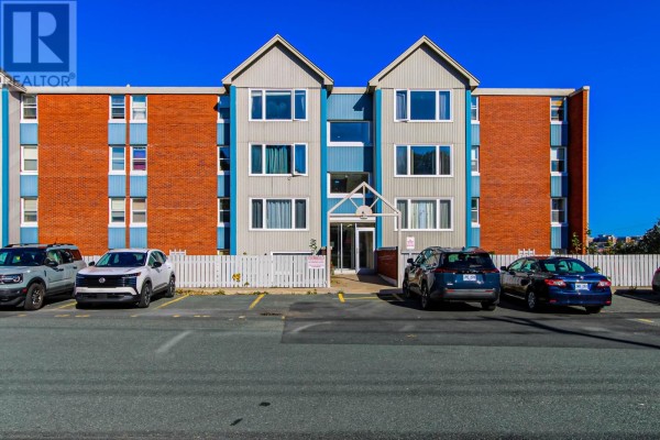 Front exterior of an apartment building with brick and light blue siding, under a clear blue sky. - 157 Forest Road Unit#65, St  John S