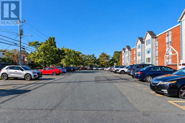 Parking lot with cars and the exterior of an apartment building along the right side. - 157 Forest Road Unit#65, St  John S