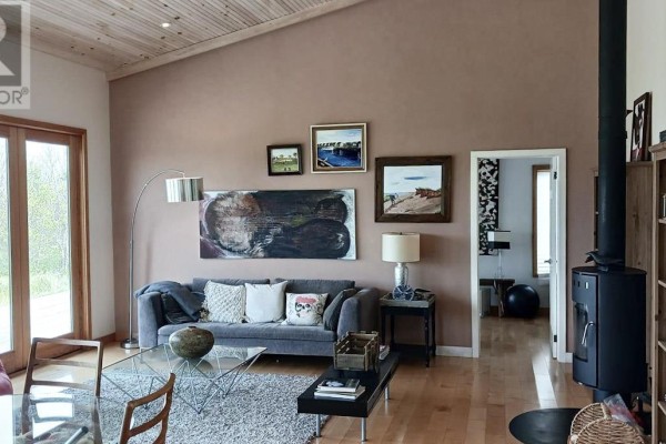 Living room with gray sofa, glass coffee table, wood floors, and a black wood stove. - 157 Trout Lake Road, West St  Peters
