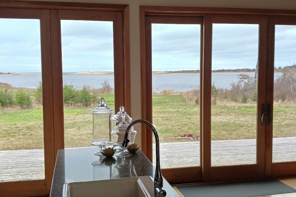 Kitchen counter with sink and glass jars, overlooking a waterfront view through wooden sliding doors. - 157 Trout Lake Road, West St  Peters