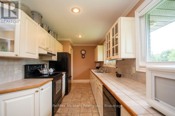 Kitchen with white cabinets, black appliances, tiled countertops, and a large window - 1571 Elm Tree Road Kawartha Lakes