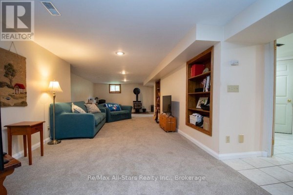 Finished basement living area with teal sofa, stove, and bookshelf - 1571 Elm Tree Road Kawartha Lakes