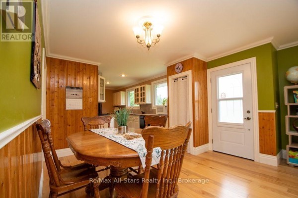 Wooden dining table and chairs, paneled walls, kitchen view, and glass door - 1571 Elm Tree Road Kawartha Lakes