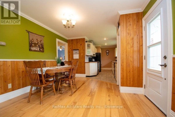Dining area with wooden table and chairs, wood paneled walls, and kitchen view - 1571 Elm Tree Road Kawartha Lakes