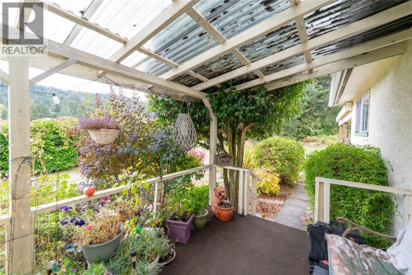 Covered porch area with plants, railings, and a view of the garden and trees. - 1571 Tatlo Rd W, Crofton
