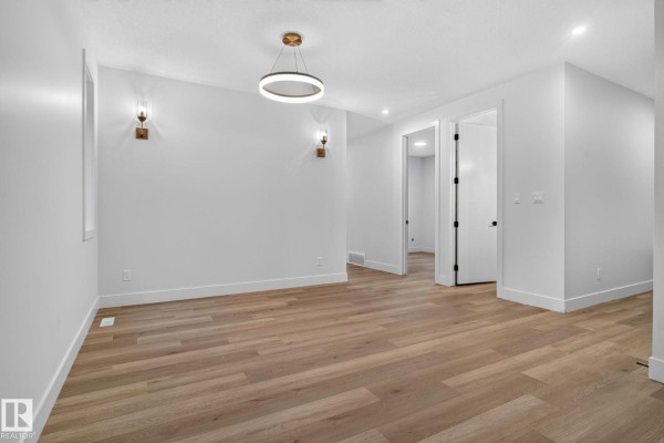 Spacious room with white walls, wood floors, and doorways leading to other rooms. - 15728 9 St Ne, Edmonton