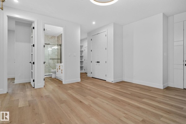 Room with white walls, wood floors, and entrances to a bathroom and closets. - 15728 9 St Ne, Edmonton
