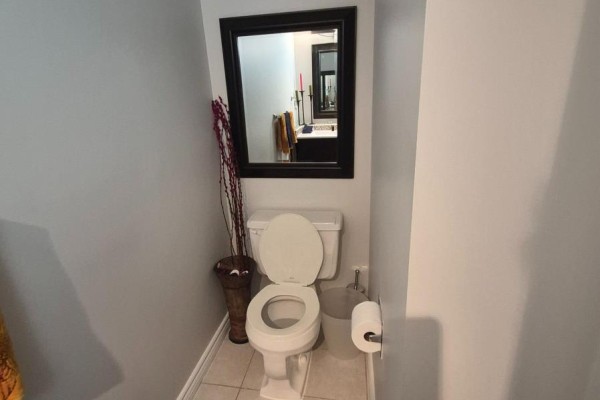 Powder room with a white toilet, toilet paper holder, and decorative vase on left. - 1576 Lassiter Terrace, Ottawa