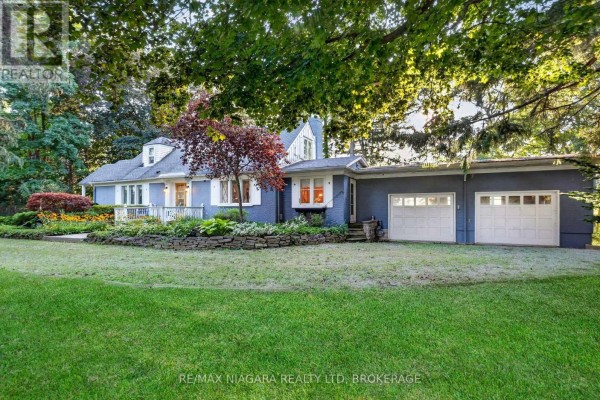 Side view of a blue ranch-style home with a white deck, stone landscaping, and a two-car garage. - 1577 Gregory Road, St  Catharines
