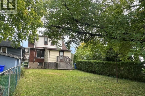 Rear view of house with beige siding, wood deck, and chain-link fence. - 1577 Moy Avenue, Windsor