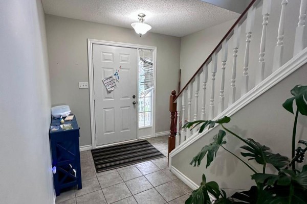 Foyer with beige tiled floor, white front door, striped doormat, and a staircase railing. - 1577 Purser Street, London East