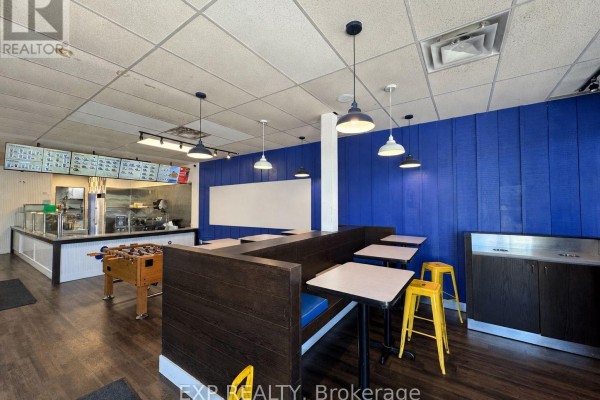 Dining area with booth seating, tables, yellow stools, and a foosball table. - 1579 Oxford Street E, London East