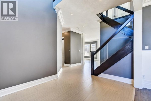Interior view of a hallway with gray walls, wood-look floors, and a glass-paneled staircase. - 158 Acton Street, Strathroy