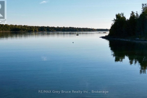Calm blue water reflects the clear sky, with forested shorelines on either side. - 158 Hobson's Harbour Drive, Northern Bruce Peninsula