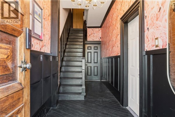 Interior hallway with black wooden floors, a staircase, and flamingo-patterned wallpaper. - 158 Hunter Street E, Hamilton