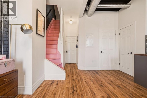 Interior space with wood-look flooring, white doors, exposed ductwork, and a pink staircase. - 158 Hunter Street E, Hamilton