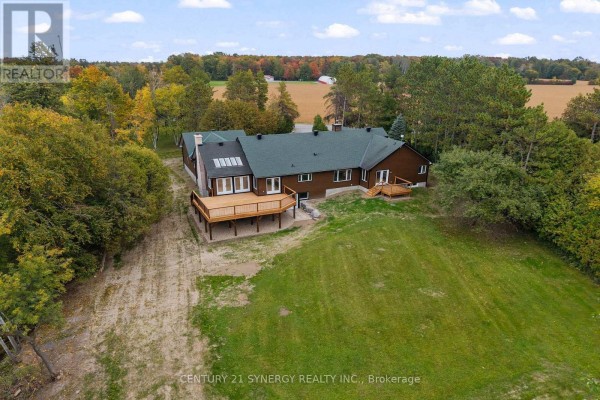 Aerial view of the rear of the house with a large wooden deck and surrounding trees and fields. - 1580 Groves Road, Russell