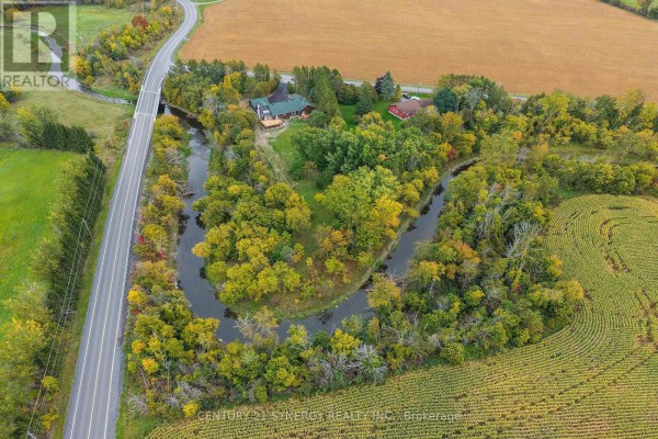 Aerial view of the property showing the house, a winding creek, a road, and agricultural fields. - 1580 Groves Road, Russell